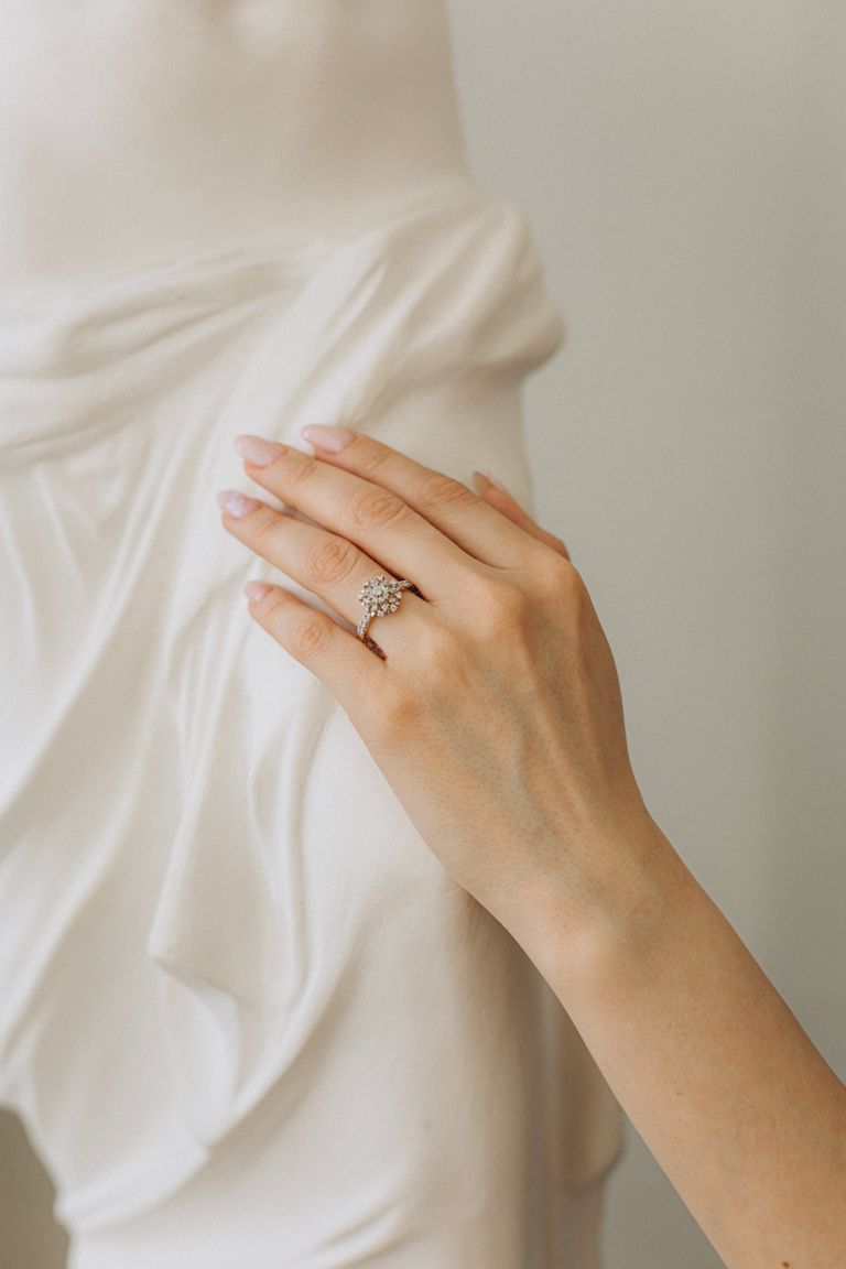 Close-up of a woman's hand with a diamond ring touching a white sculpture.